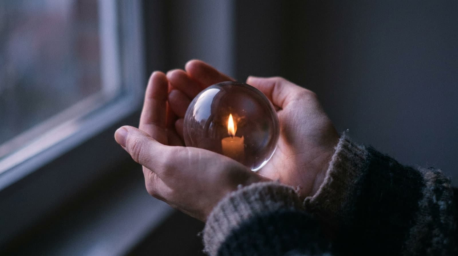 Zwei Hände halten eine Glaskugel, in der sich eine Kerze spiegelt